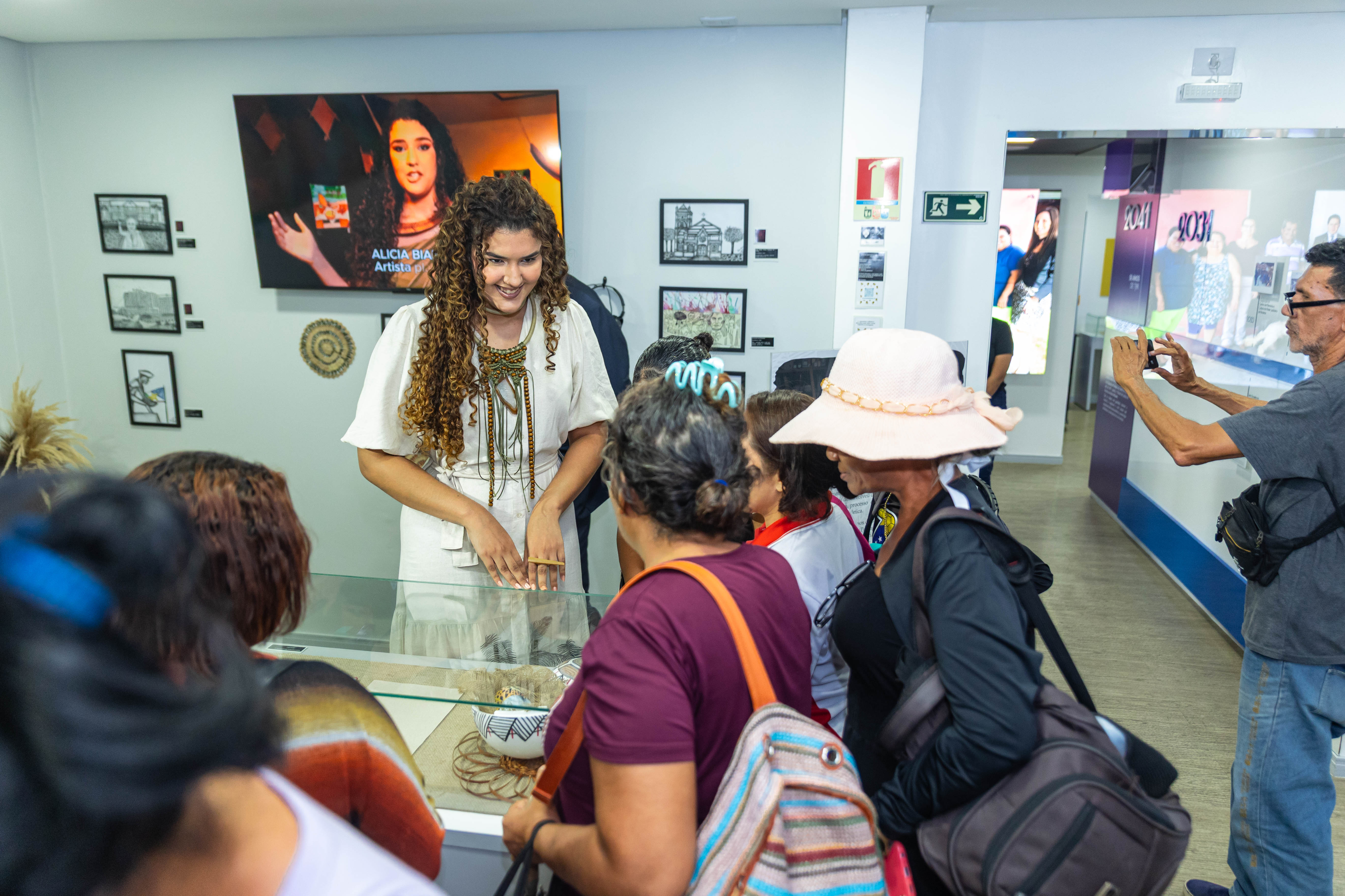 Artista interagindo com o público em uma exposição sobre seu trabalho ou cultura regional, destacando seu papel como criadora. VArtista interagindo com o público em uma exposição sobre seu trabalho ou cultura regional, destacando seu papel como criadora.