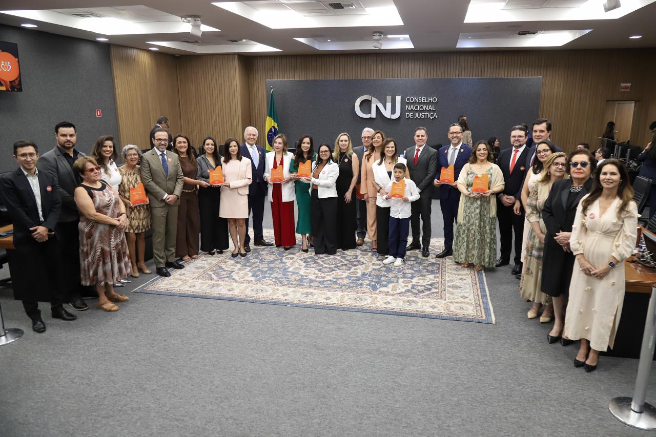 imagem colorida de um grupo grande de pessoas posando em pé em um evento solene e formal em um auditório da premiação.  imagem colorida de um grupo grande de pessoas posando em pé em um evento solene e formal em um auditório da premiação.