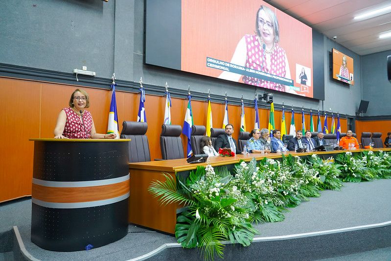Foto 2: Imagem colorida da Solenidade de entrega da Comenda "Orgulho de Roraima" com a Juíza Auxiliar da presidência Lana Leitão, posando para fotografia falando no púlpito. A mesa diretora conta com diversas autoridades. Foto 2: Imagem colorida da Solenidade de entrega da Comenda "Orgulho de Roraima" com a Juíza Auxiliar da presidência Lana Leitão, posando para fotografia falando no púlpito. A mesa diretora conta com diversas autoridades.