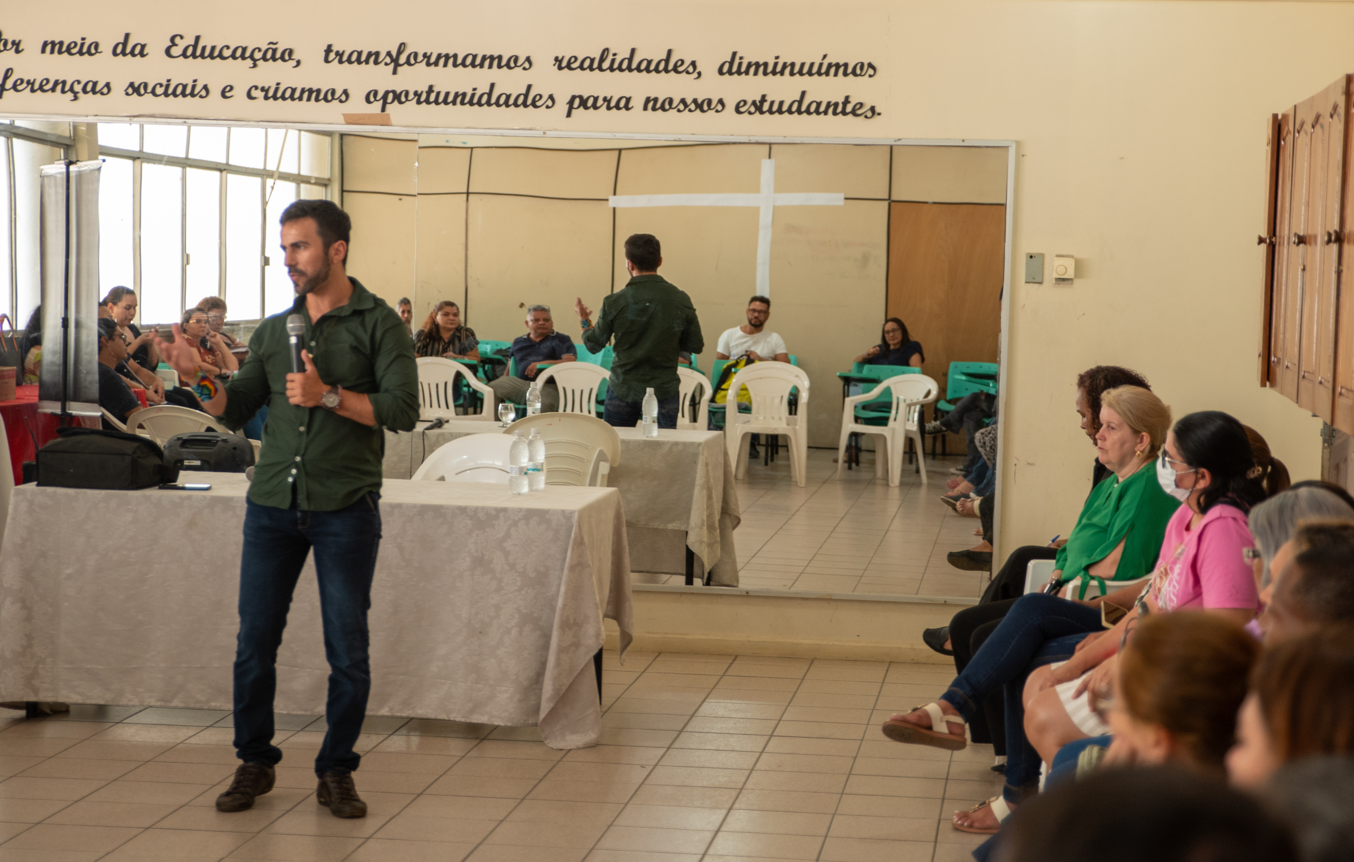 Foto colorida mostra o pedagogo Fernando Alves à esquerda discursando para os presentes que se encontram sentados em cadeiras à direita da imagem.