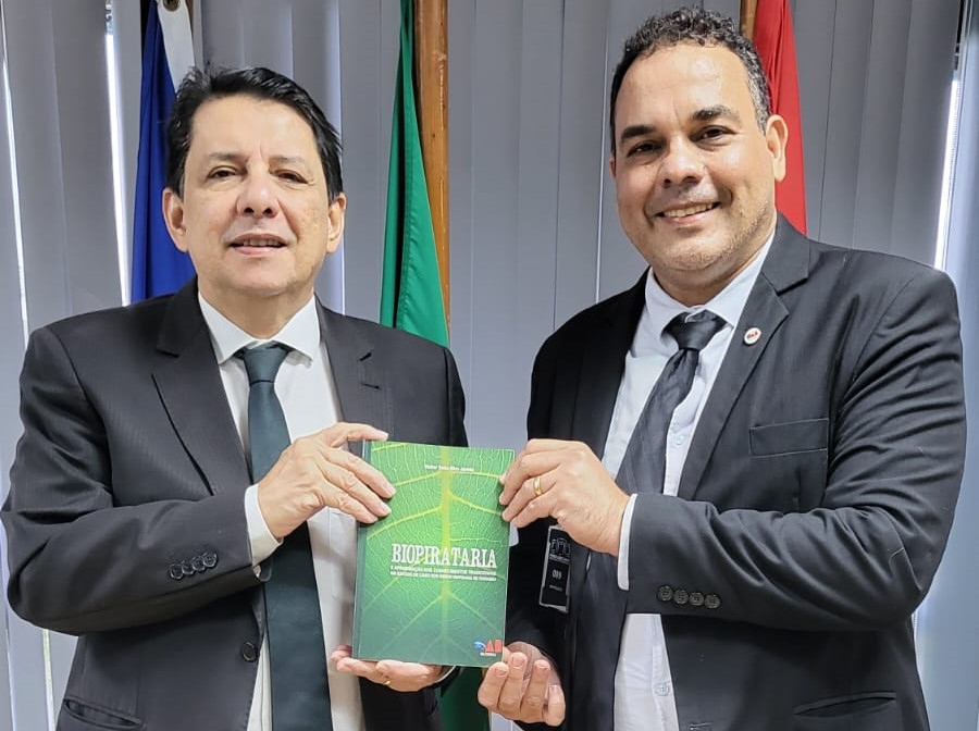 Imagem colorida do O presidente do Tribunal de Justiça de Roraima, desembargador Jésus Nascimento e do o advogado Walker Sales Silva Jacinto, segurando um livro .