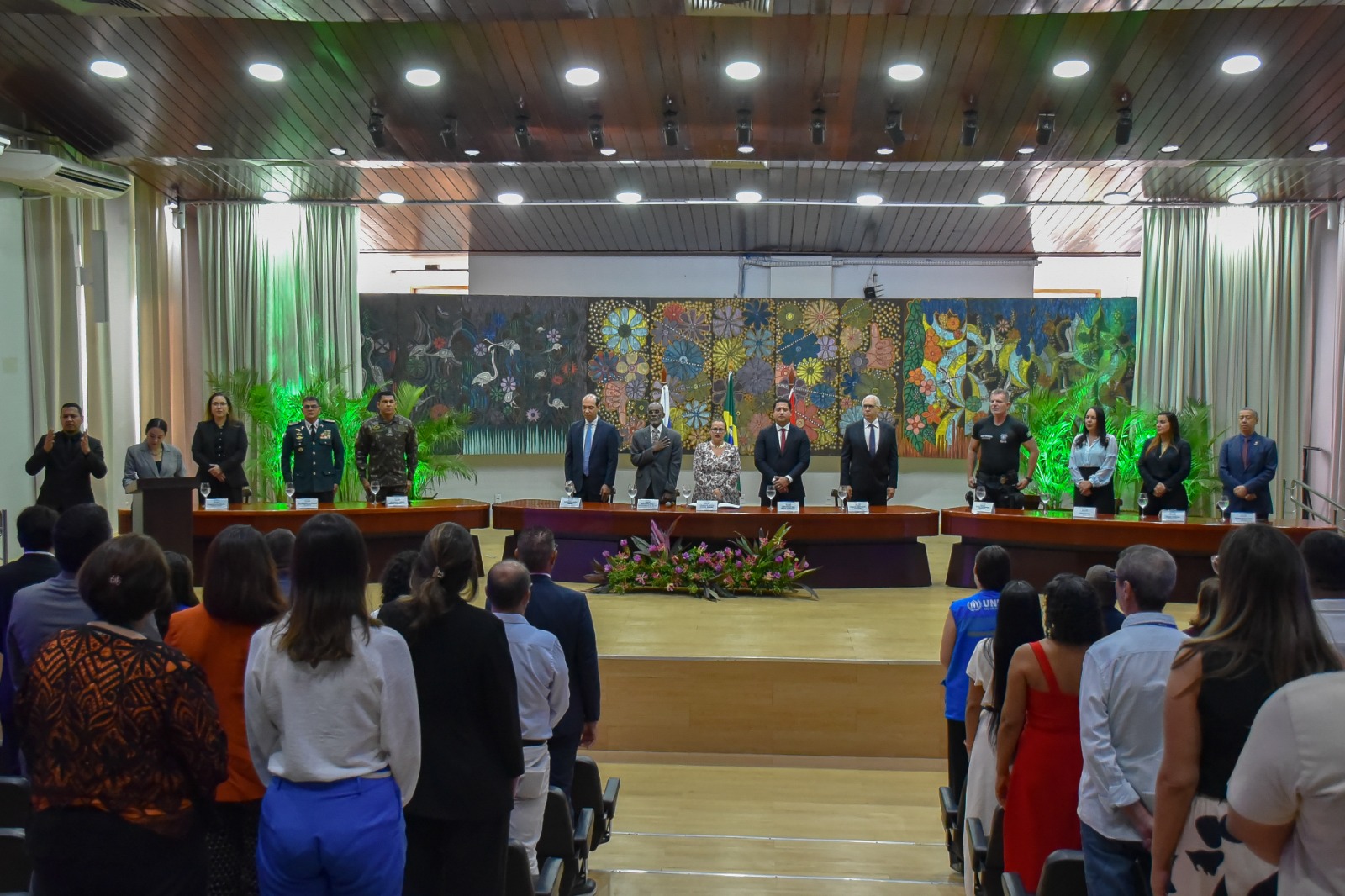 Foto colorida mostra os presentes de pé durante canto do hino nacional.