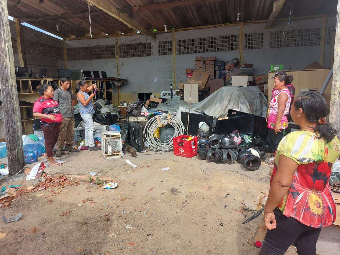 Foto colorida mostra seis pessoas da  Associação Catadores de Materiais Recicláveis Terra Viva, observando materiais reciclados.  Ao redor vários materiais reciclados.