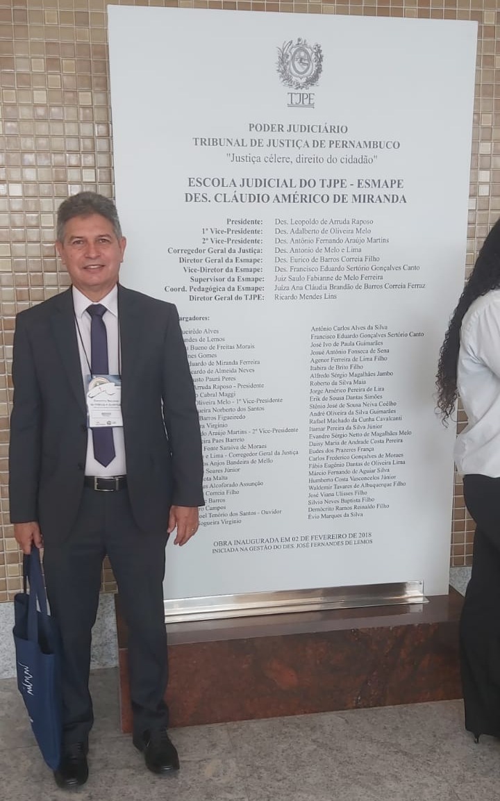 foto colorida na vestical do juiz Parima Dias Veraspousando para foto ao lado da placa de tombamento da Escola Judicial do TJPE