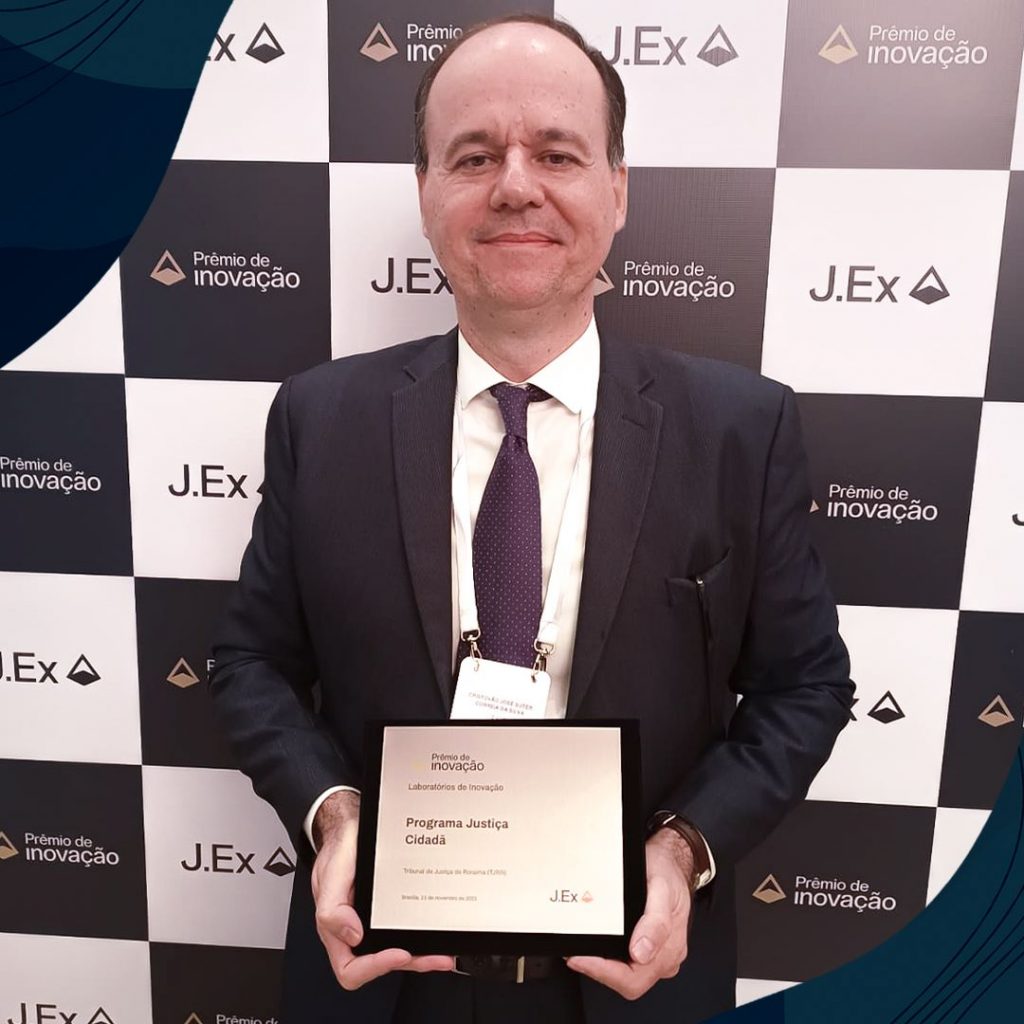 Imagem 3: Foto colorida mostra o coordenador do Justiça Cidadã, desembargador Cristóvão Suter, posando para a foto segurando placas de metal que simbolizam o prêmio de inovação 2023.