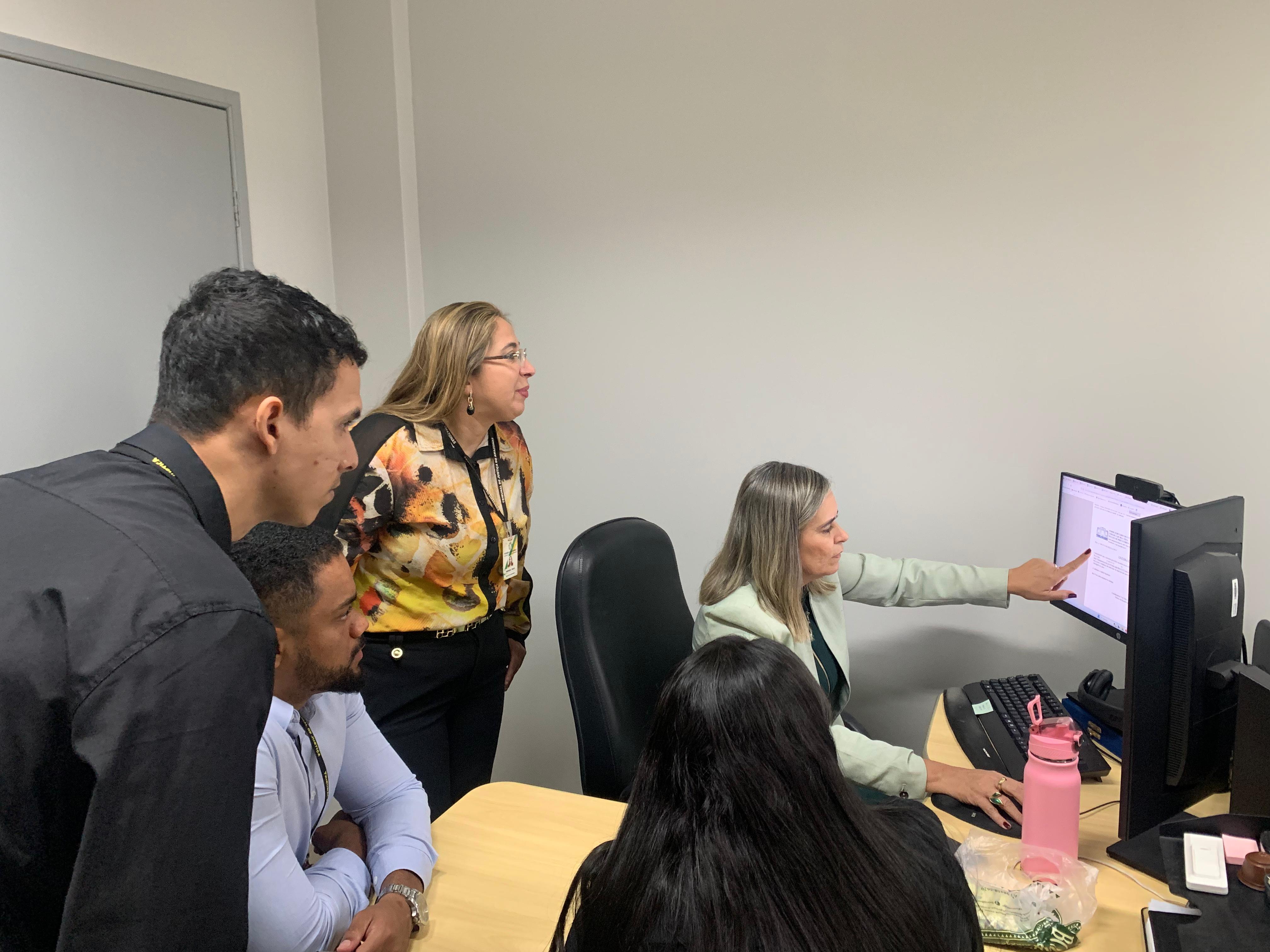 Imagem colorida mostra a coordenadora do NUPREC/TJRR, Valdira Silva, mostrando algo no computador para a secretária da Central de Precatórios, Andreia Souza Pinto, o assessor do juiz, Roberto Brito Neto, o chefe do Setor de Cálculos, Joyce Sigadilha e o técnico da Tecnologia da Informação, Erick Bolorini, durante visita institucional.