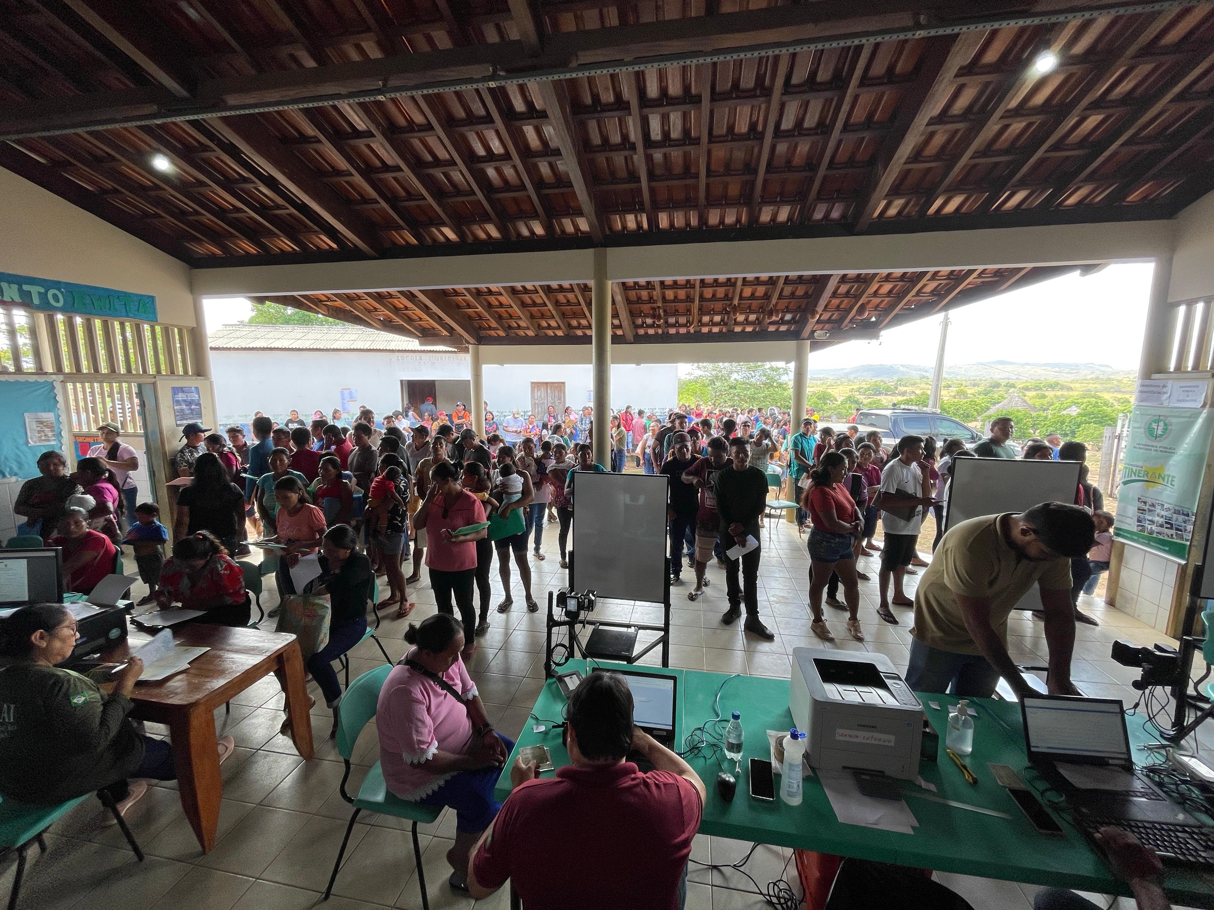 Imagem colorida de ângulo aberto mostra o local de atendimento da Justiça Itinerante, com várias pessoas esperando a vez.