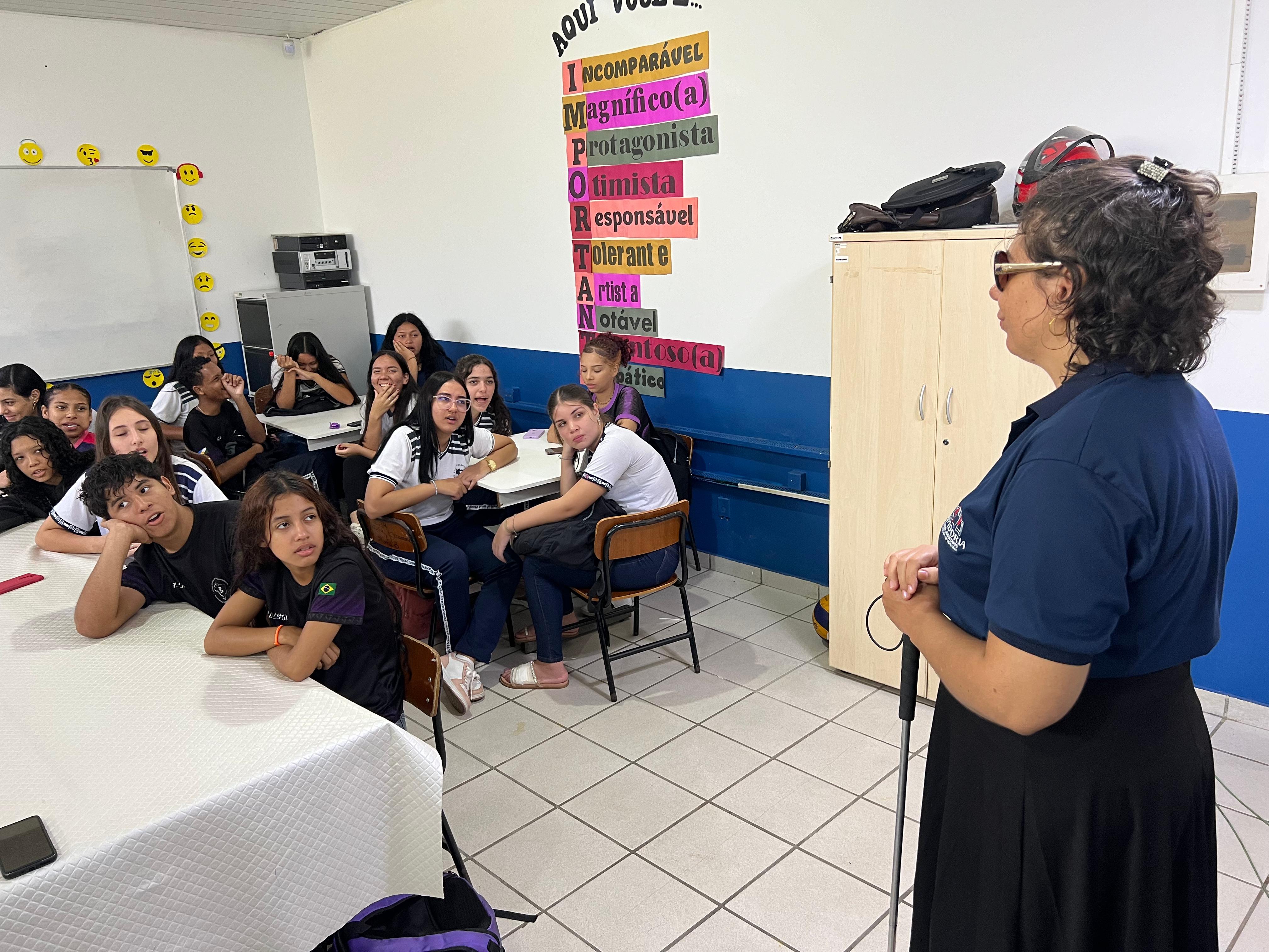 foto colorida em sala de aula com alunos sentados e uma servidora do TJRR falando a frente