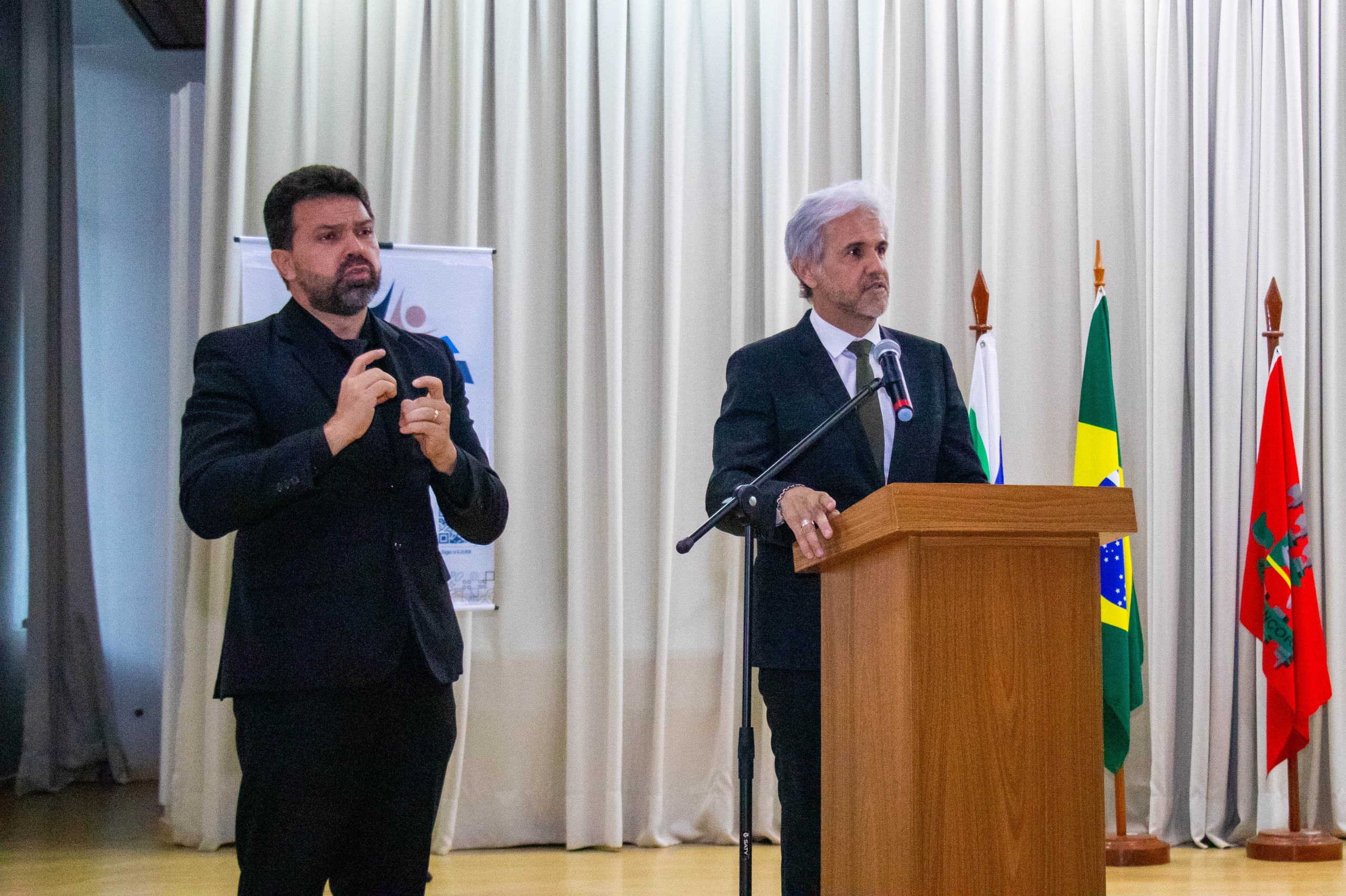 foto colorida do juiz titular do 2º Juizado de Violência Doméstica e Familiar, Jaime Plá Pujades falando no púlpito ao lado do interprete de libras