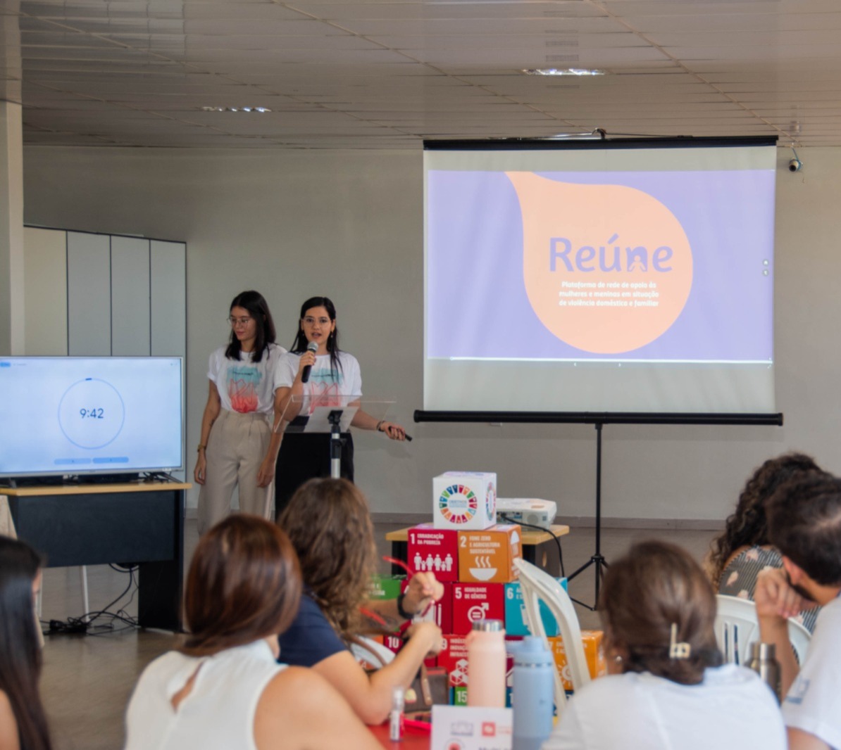 foto colorida de uma equipe composta por duas mulheres apresentando o projeto