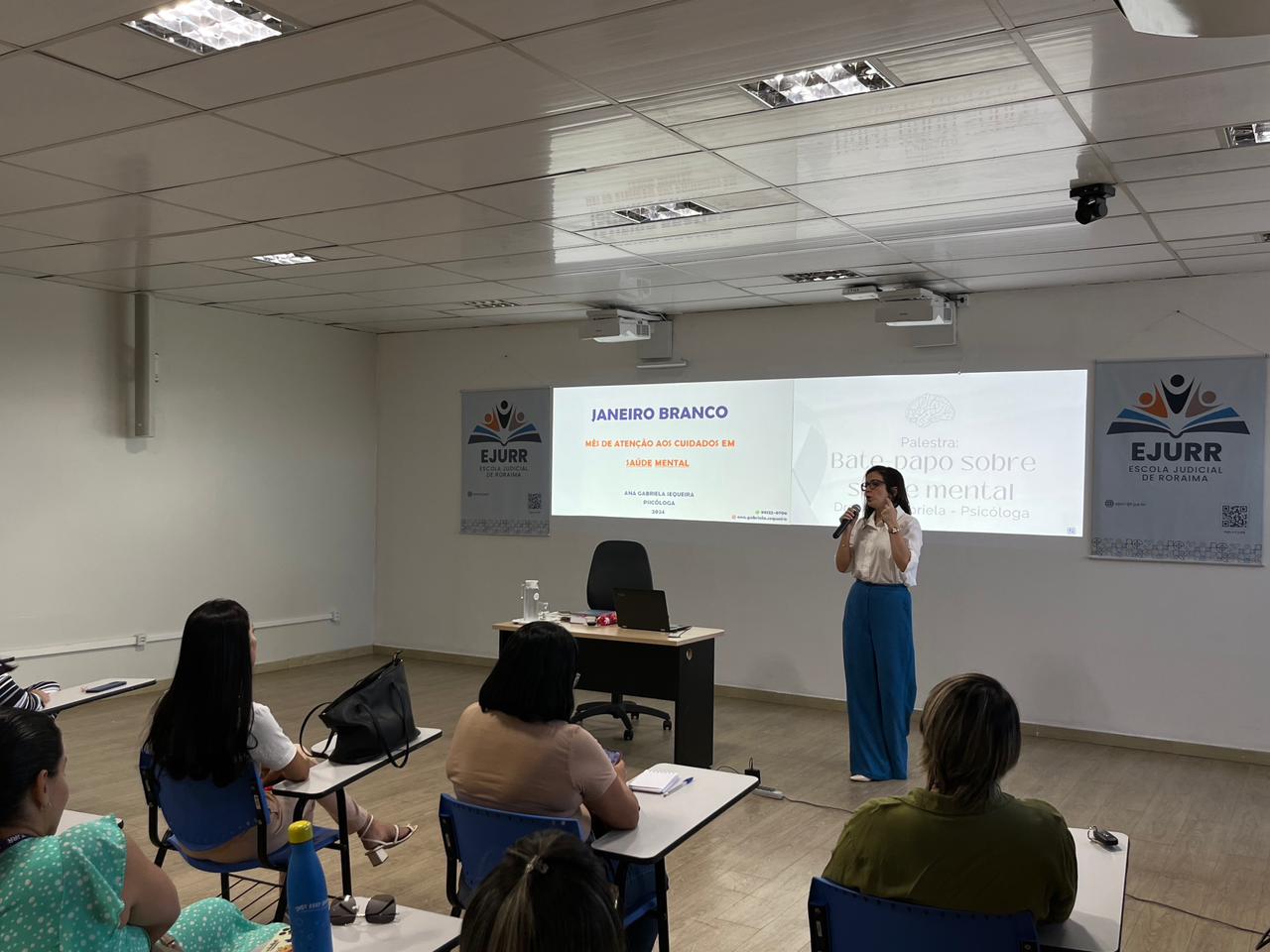 foto colorida de uma uma mulher palestrando para um turma de pessoas