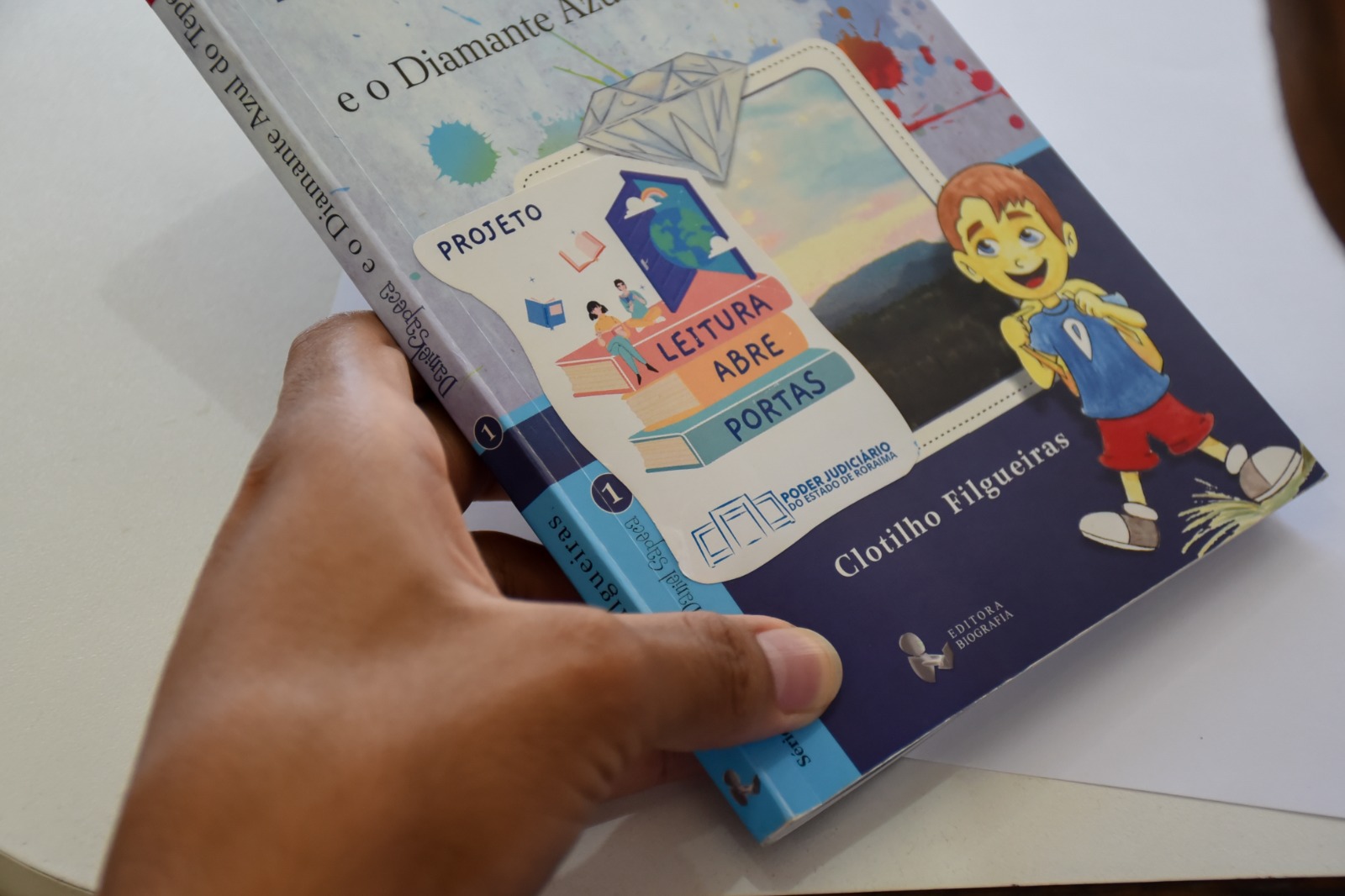 foto colorida de uma mão segurando o livro