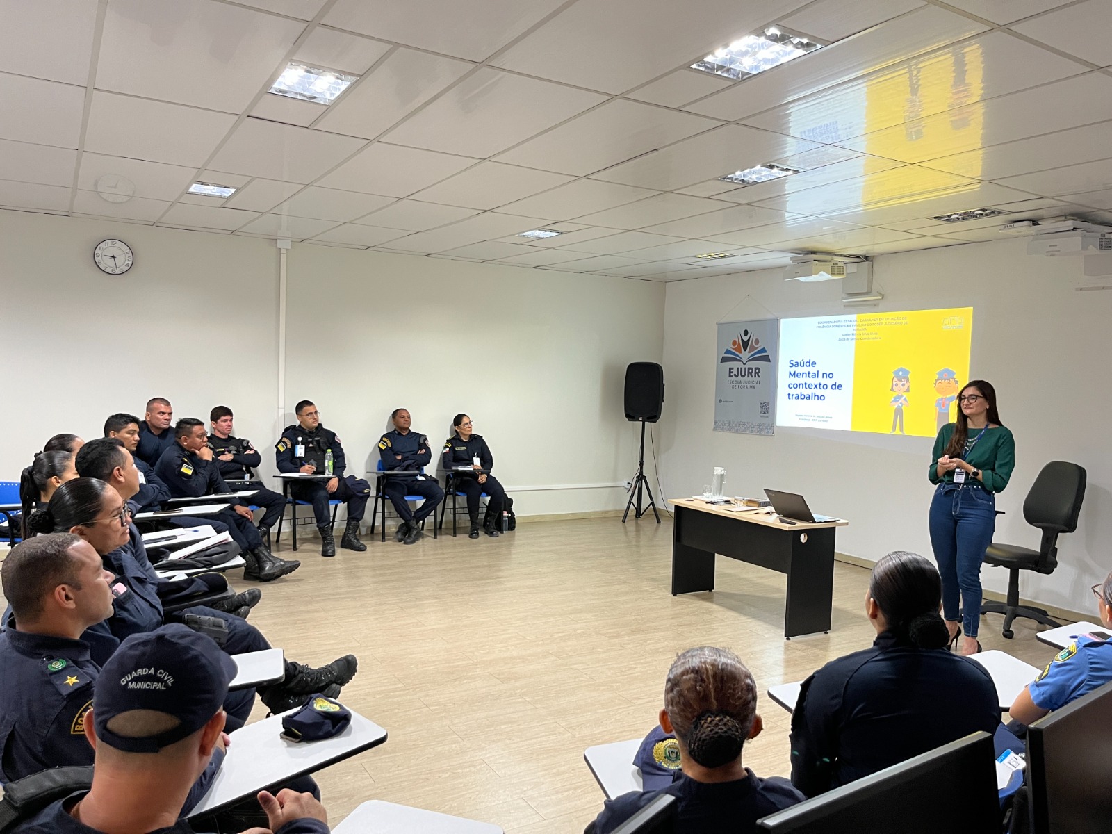 foto colorida de uma servidoras do TJRR a frente da sala e 17 policias sentados em cadeiras escolares