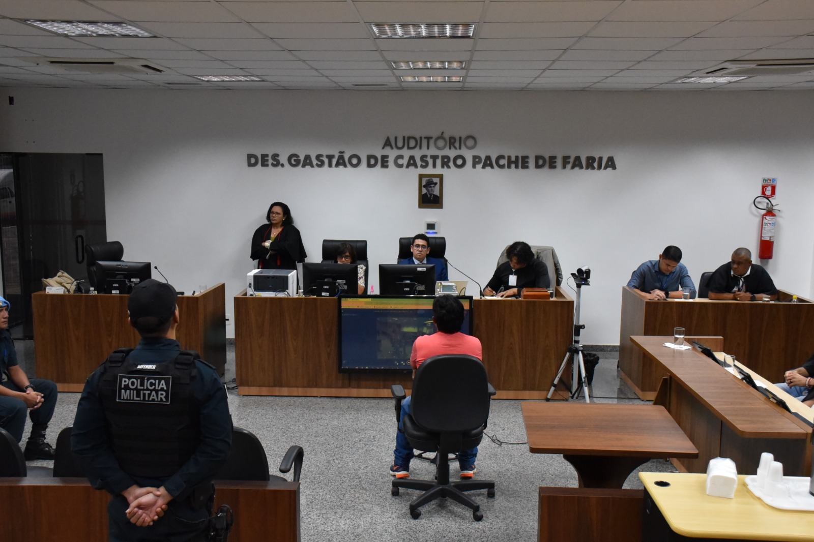 Imagem 1: Foto colorida de um audiório com uma pessoa sentada ao centro, de frente para outras que estão sentadas trabalhando. Abaixo, está escrito "PRIMEIRO SEMESTRE - Tribunal de Justiça de Roraima divulga pauta de júris e lista de jurados convocados"