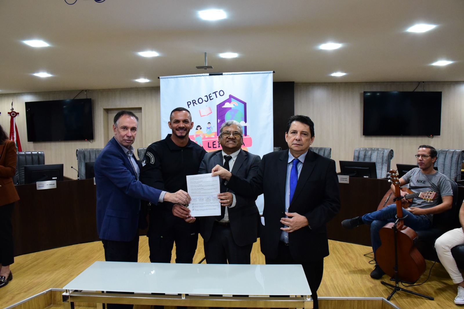 foto colorida com dois representantes do acordo e ao lado direito deles está o desembargador Jésus Nascimento, enquanto ao lado esquerdo está o desembargador supervisor do GMF, Almiro Padilha. Todos estão posando para foto segurando o acordo de cooperação assinado.