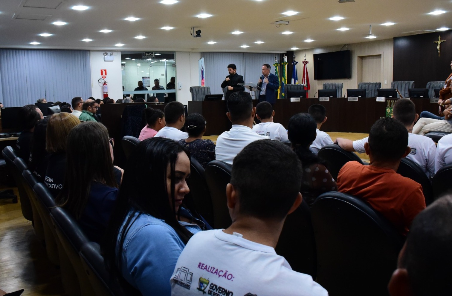 foto colorida dentro do tribunal pleno mostrando o público presente durante a celeridade da assinatura do termo, ao fundo é possível ver no púlpito de vidro ao lado de um intérprete de libras o desembargador, supervisor do GMF, Almiro Padilha, falando ao microfone.