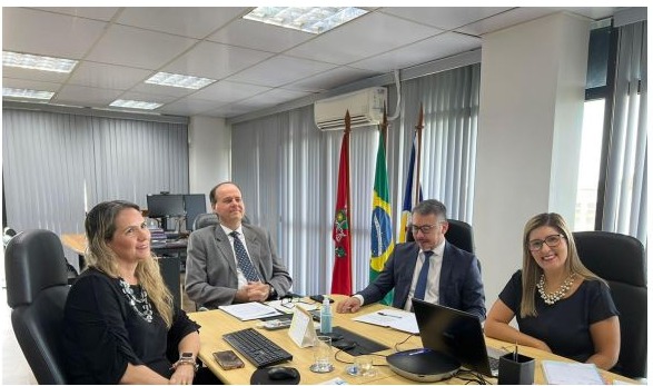 Imagem colorida em formato retangular mostra o desembargador Cristóvão Suter em uma sala de reuniões com um servidor e duas servidoras do TJRR.