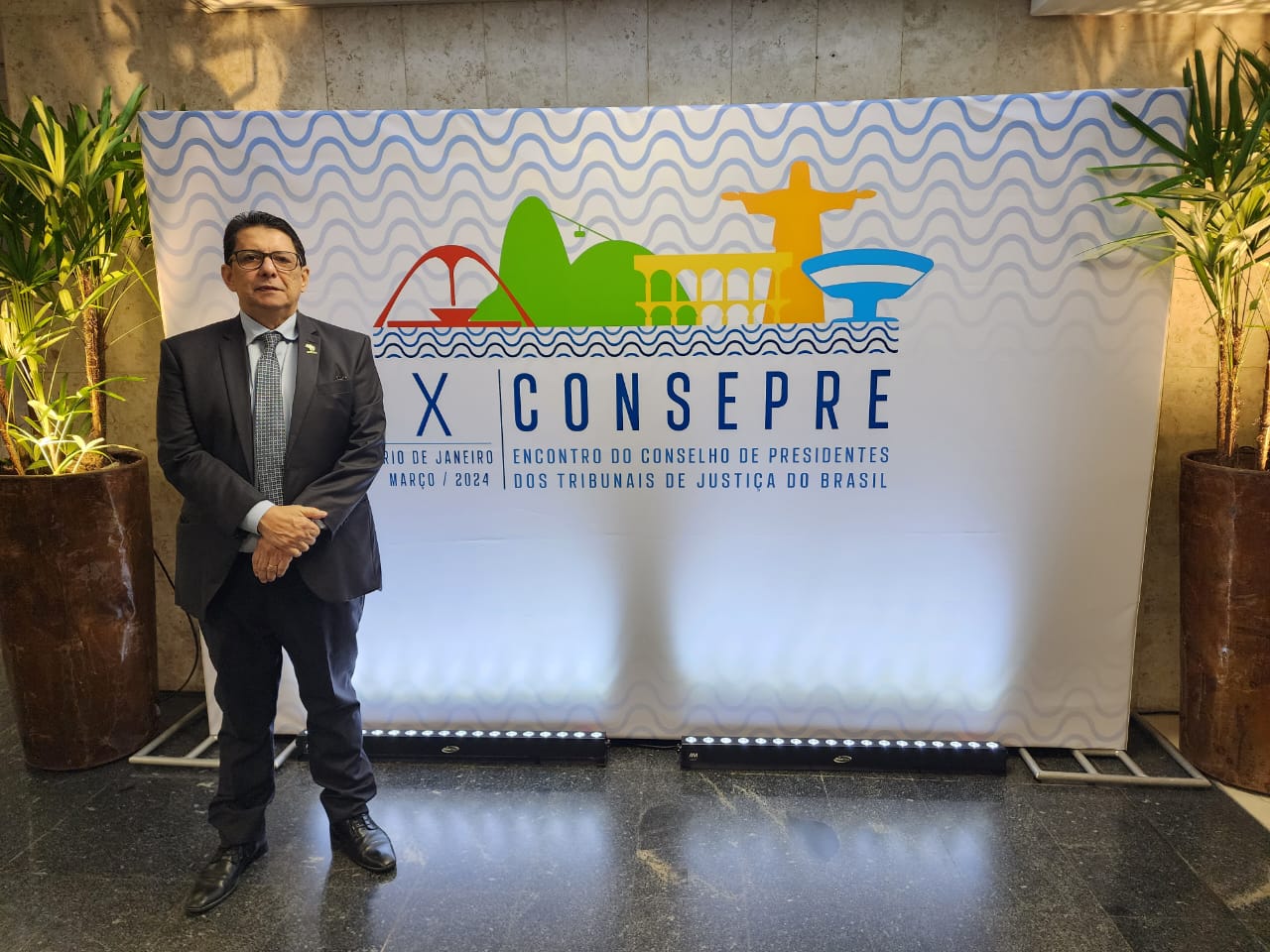 Foto colorida mostra o presidente do Tribunal de Justiça de Roraima, desembargador Jésus Nascimento, posando para foto com o banner do evento ao fundo.