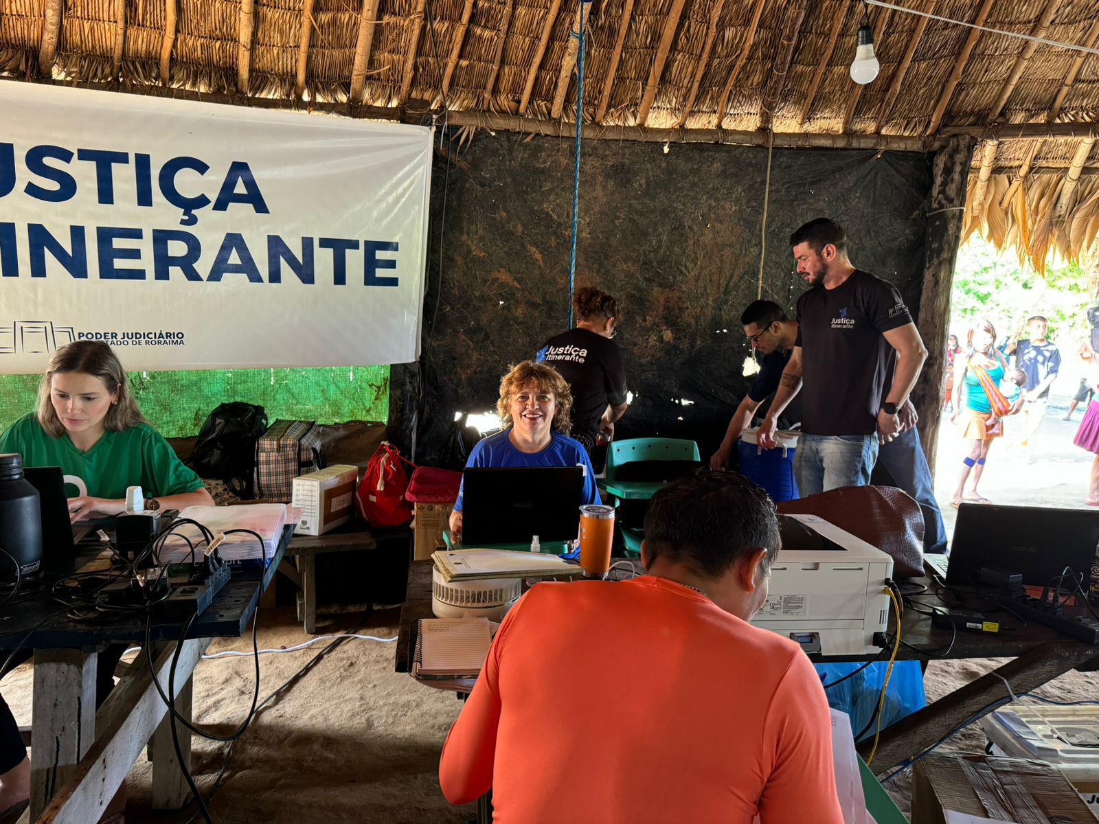 Imagem colorida mostra seis pessoas, entre elas servidores do TJRR, que atuam na Vara da Justiça Iitnerante do TJRR, e indígenas durante atendimento da Justiça Itinerante em comunidade indígena do interior do Estado de Roraima. 