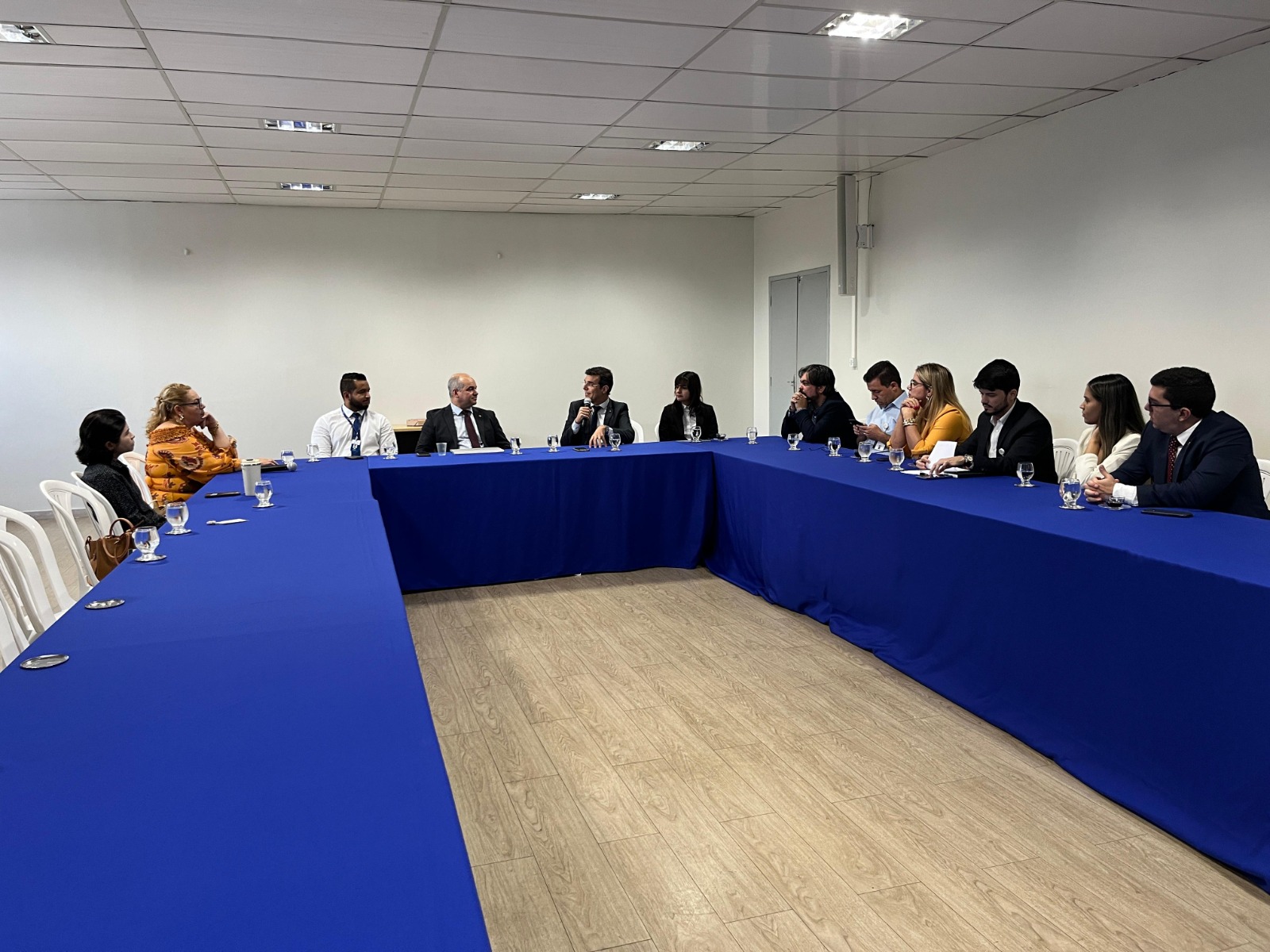 foto colorida de servidores sentados ao redor de uma mesa, com toalha azul, em reunião