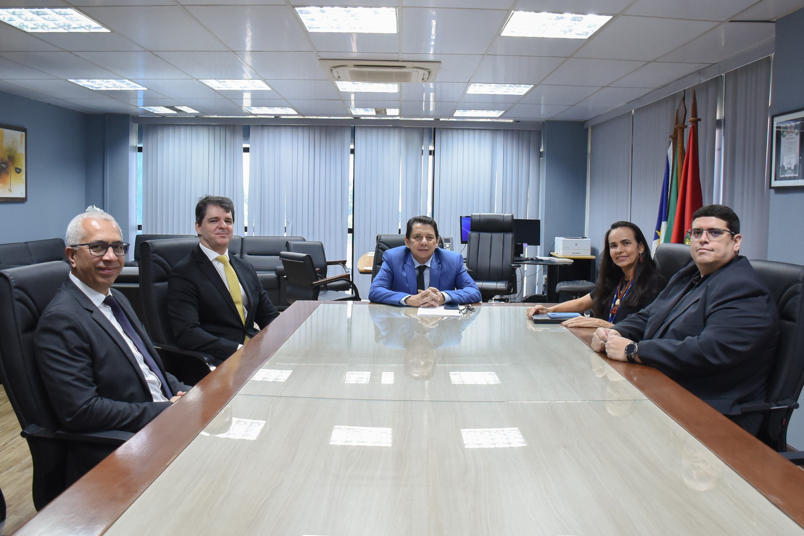 Imagem colorida mostra mesa, com os presentes superintendente regional da Polícia Federal em Roraima, Ronaldo Guilherme Campos, o delegado Carlos Henrique Macedo, diretor regional executivo no Estado e os assessores da presidência, Katia Lima e Alexandre Ferreira sentados em torno dela posando para foto.