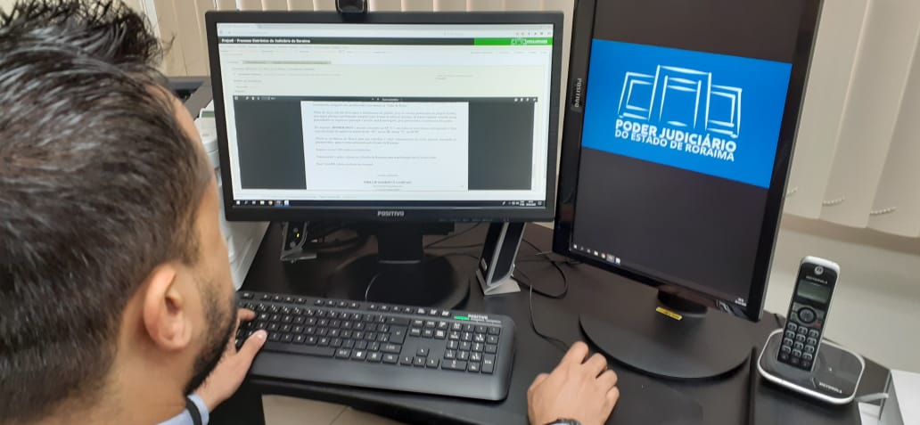 Um homem está sentado a mesa olhando para a tela do seu computador