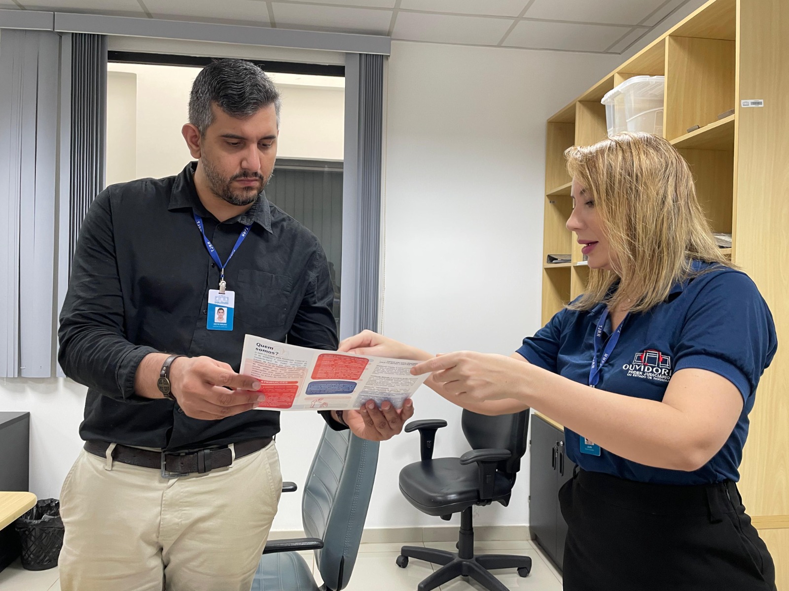 Imagem colorida mostra a servidora do CEAVCAI, Isabelle Cristina, mostrando o card do CEAVCAI para outro servidor.