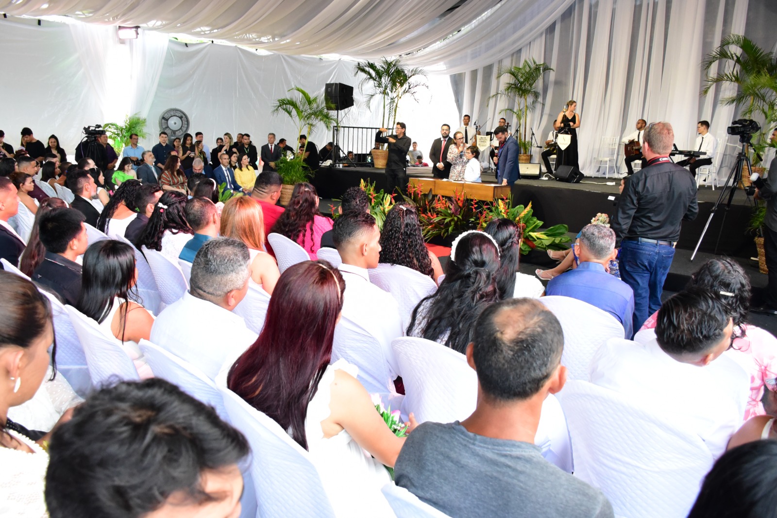 Foto colorida mostra casais sentados em cadeiras durante o evento.