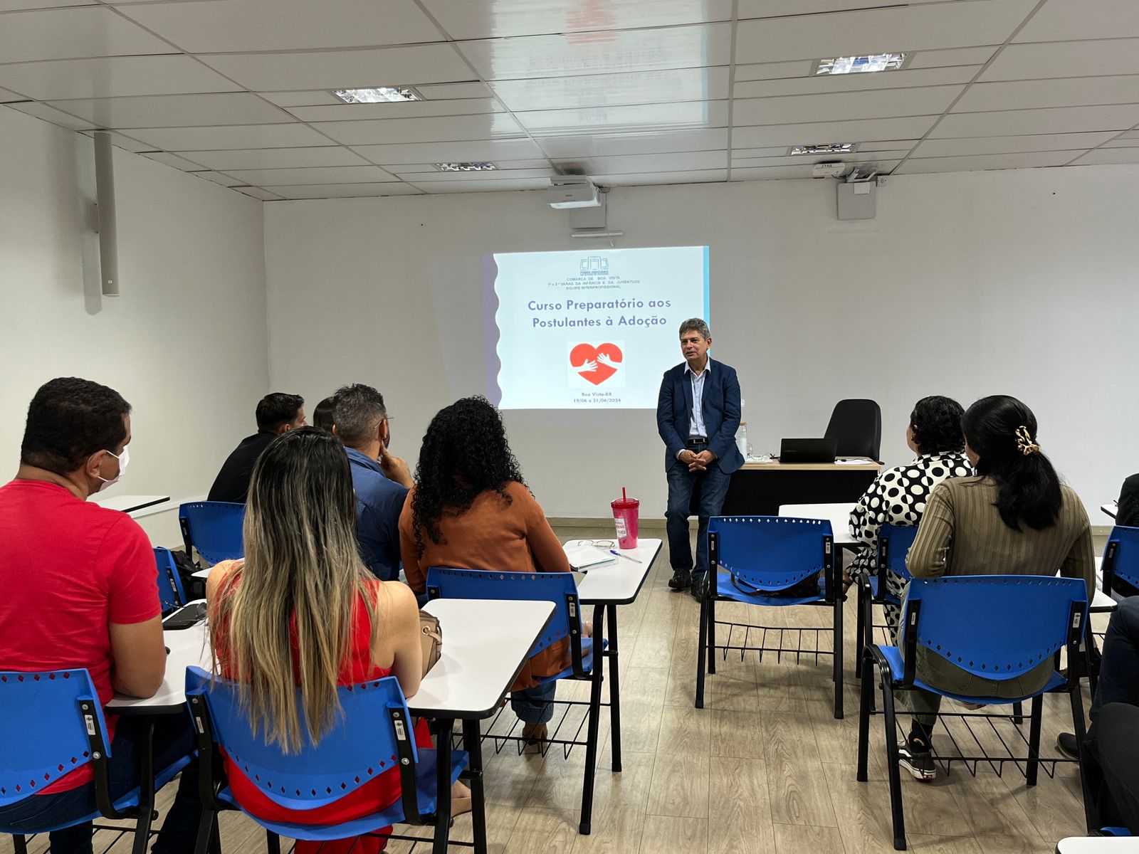 Imagem colorida mostando pessoas sentadas em fileiras assistindo palestra ministrada pelo o juiz titular da 1ª Vara da Infância e Juventude, Parima Dias Veras,