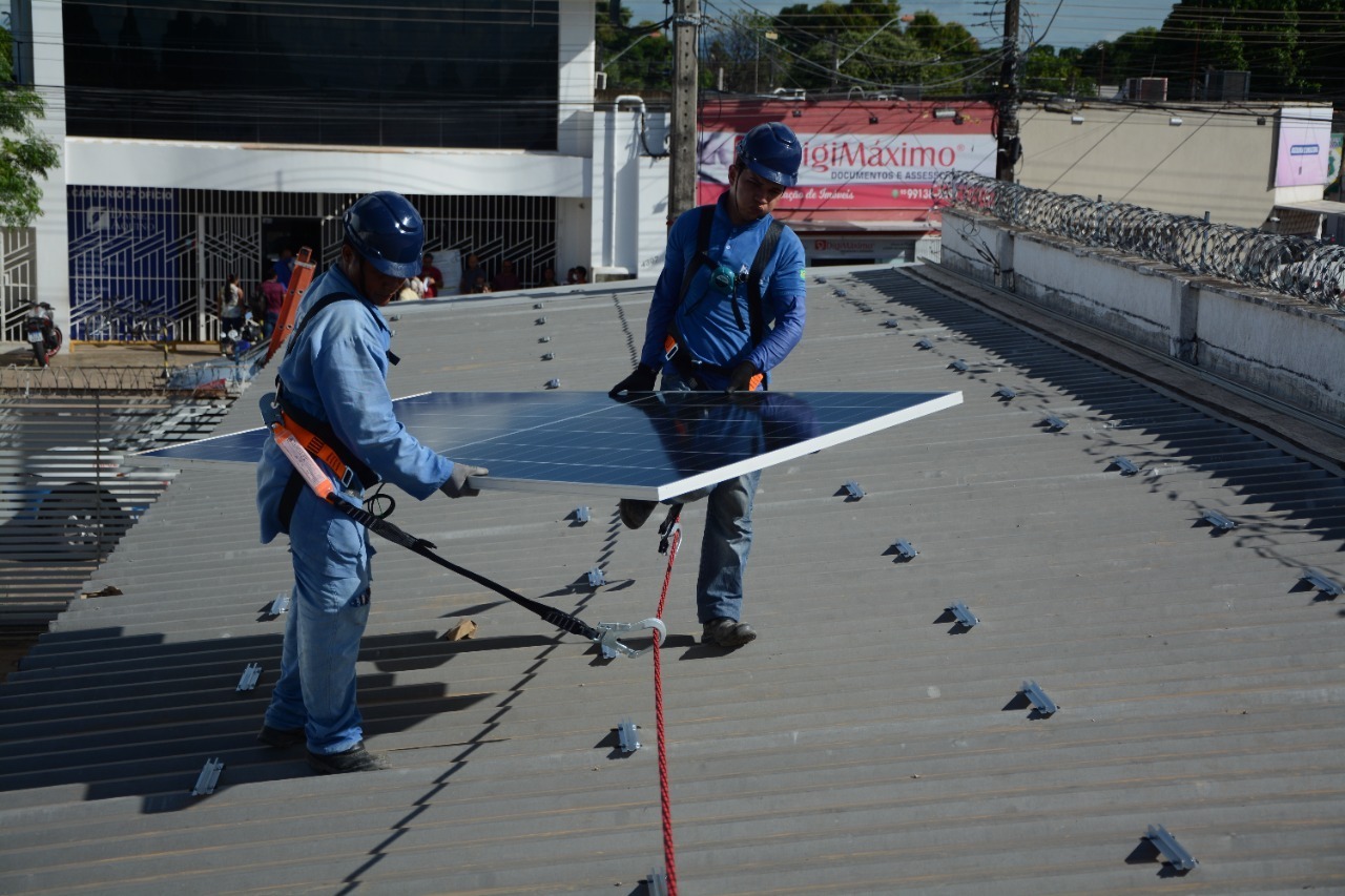 Imagem colorida mostrando dois homens levando uma placa solar