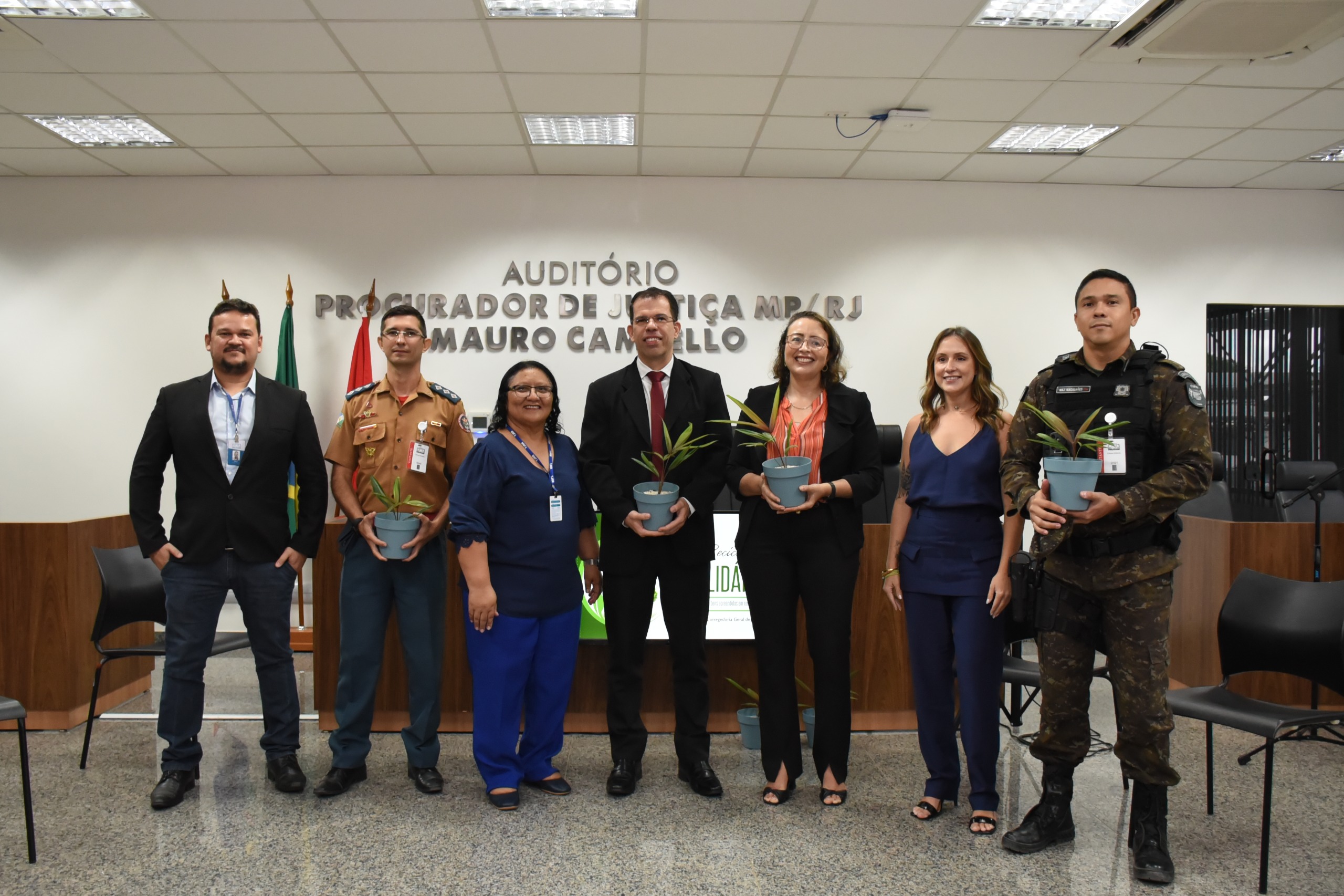 Imagem colorida mostrando pessoas posando para foto e segurando mudas de plantas, entre elas a juiza Lana Leitão e servidores do TJRR