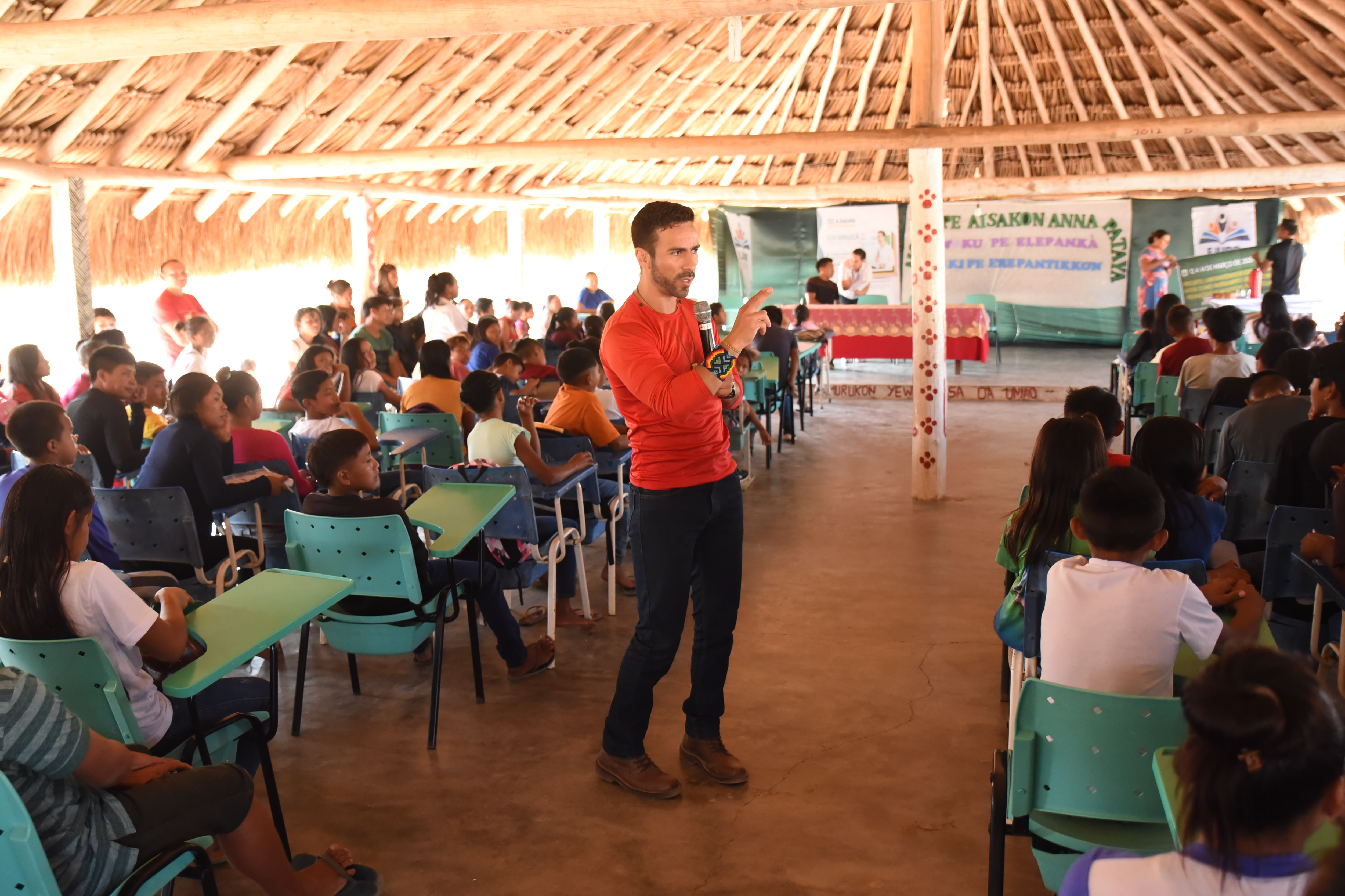 Foto colorida mostra o pedagogo Fernando Alves conduzindo uma palestra, dentro de uma sala da Escola Estadual Indígena Júlio Pereira, que mostra alunos sentados em cadeiras ao fundo.