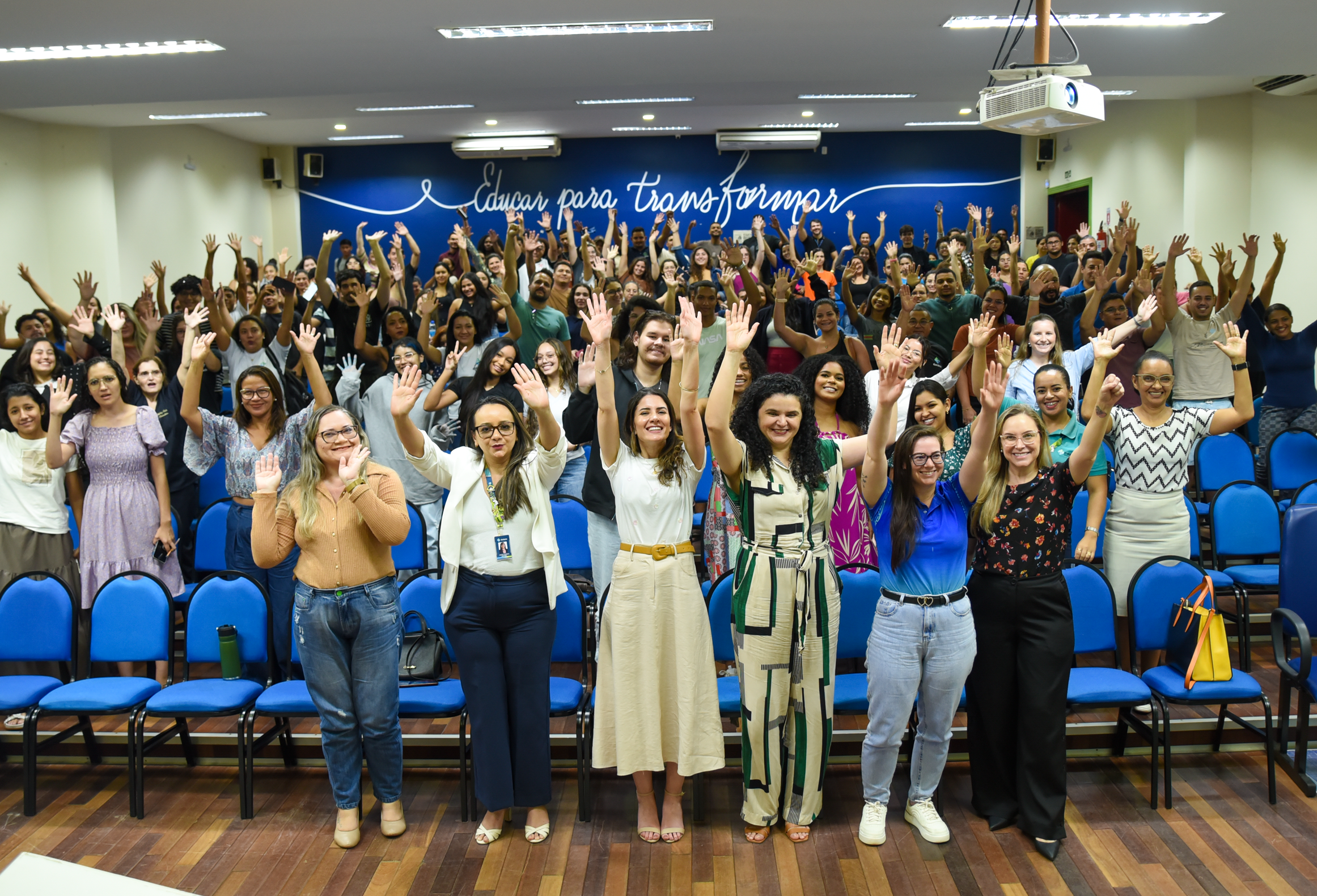 foto colorida de pessoas no auditório levantando a mão