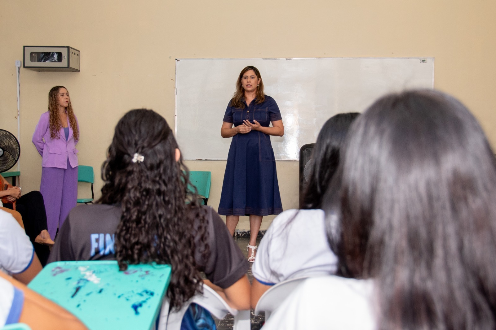 A imagem colorida mostra a juíza Rafaelly Lampert em palestra numa sala de aula durante o evento.