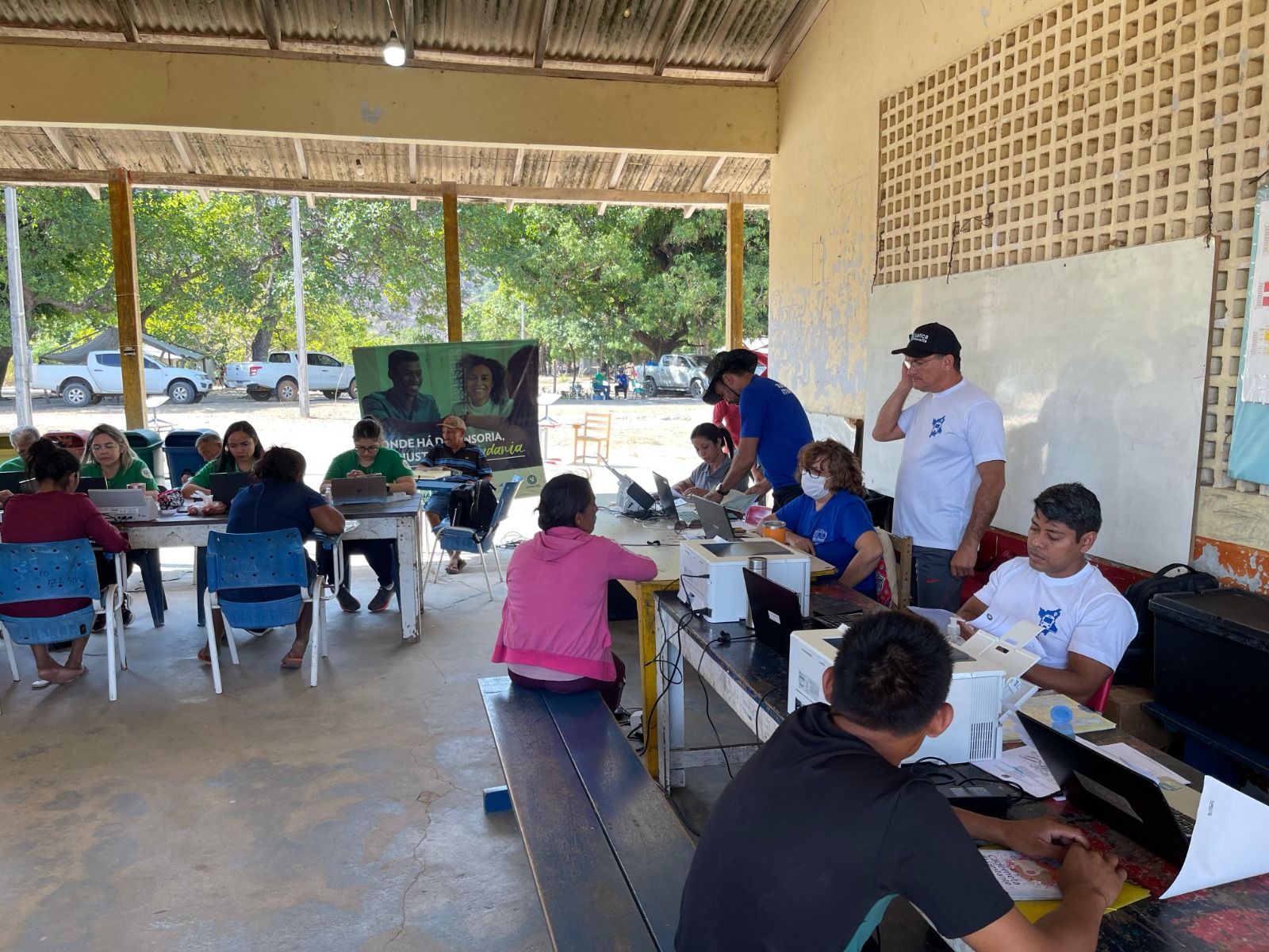 Foto colorida mostra duas mesas, com representantes da Justiça Itinerante e pessoas recebendo atendimento.