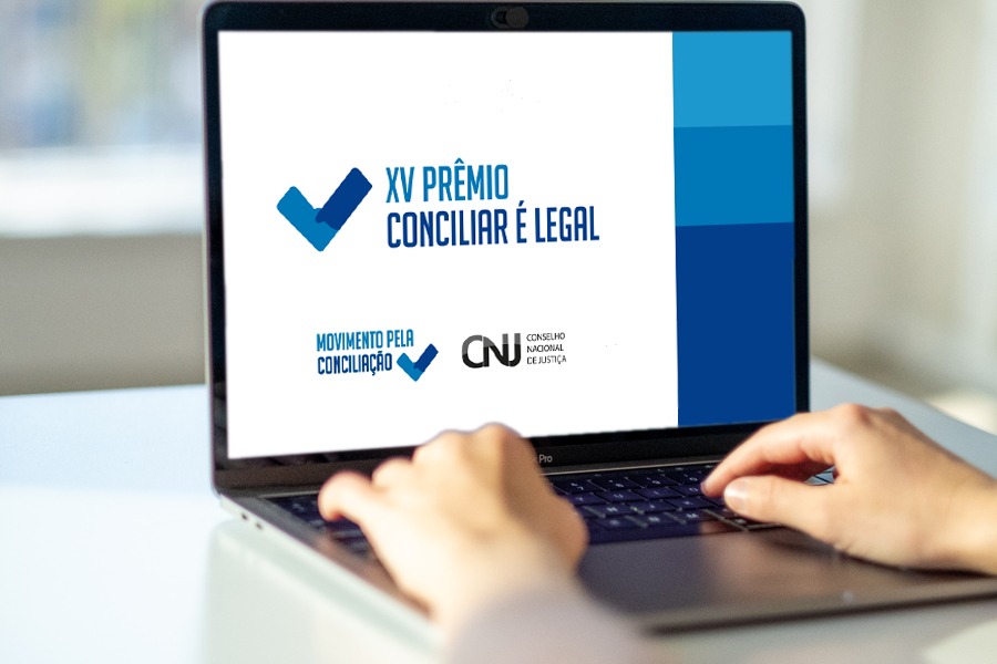 foto ilustrativa colorida de uma pessoa mexendo no notebook na tela possui escrito XV Prêmio Conciliar É Legal, do Conselho Nacional de Justiça (CNJ).